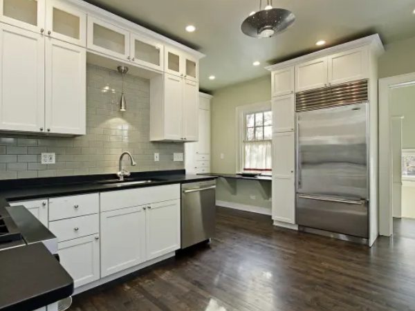 A kitchen with white cabinets and wood floors.