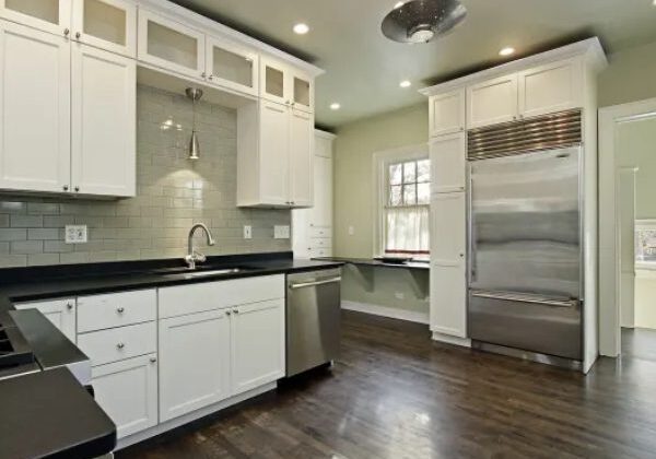 A kitchen with white cabinets and wood floors.